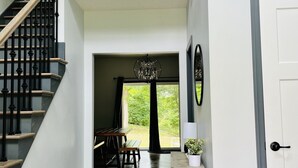 A spacious hallway with a wooden staircase, a dining area with a table and chairs, and a view of the outdoors through a large window. - Private 5 bedroom house in the heart of Laurel highlands! (Normalville)