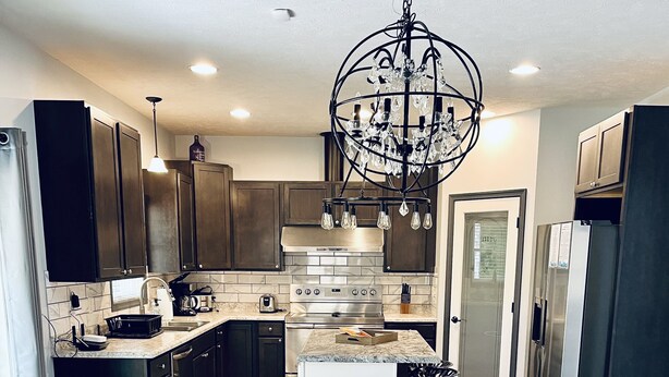 A modern kitchen with dark cabinets, a central island, a chandelier, and a wooden dining table. - Private 5 bedroom house in the heart of Laurel highlands! (Normalville)