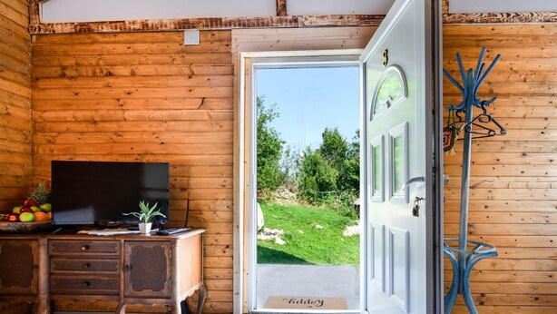 A wooden interior with a television on a wooden desk, a door leading outside, and a metal coat rack.
