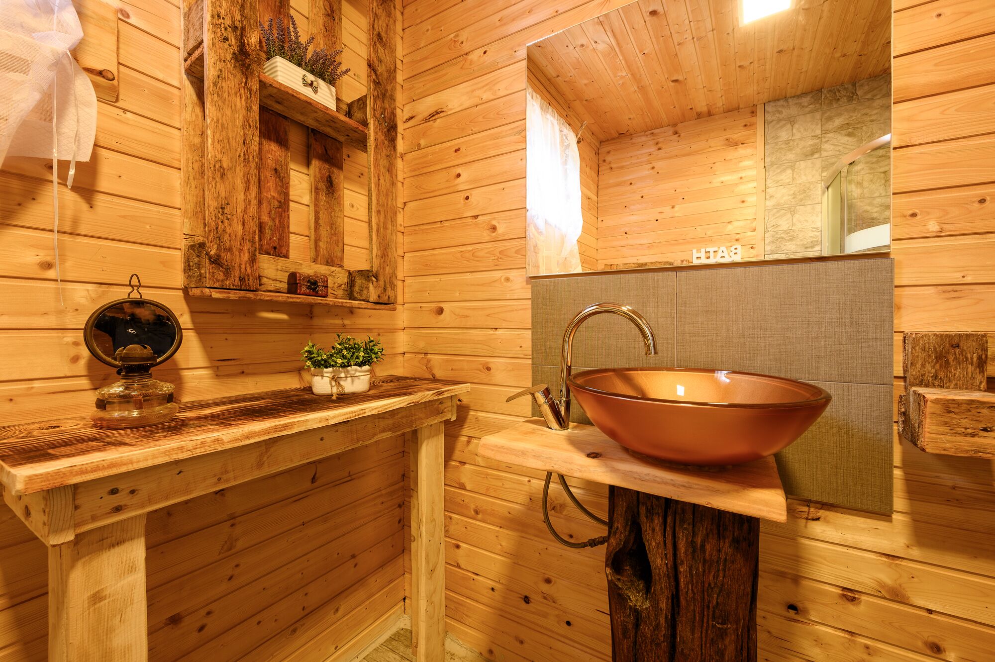 A wooden cabin bathroom with a copper sink, wooden shelves, and a mirror.