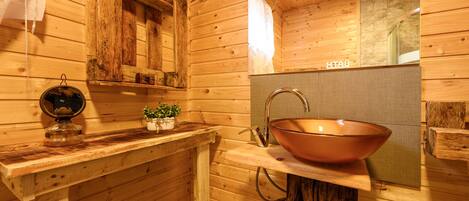 A wooden cabin bathroom with a copper sink, wooden shelves, and a mirror.