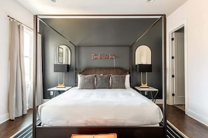 Un lit à baldaquin avec une tête de lit sombre, deux tables de chevet avec des lampes et un panneau néon au-dessus du lit.