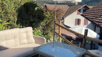 Une terrasse dotée de meubles en osier, d’une table en verre et de parasols blancs.
