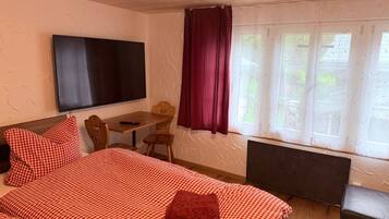 Une chambre à coucher avec un lit, un bureau, une chaise, un téléviseur et une fenêtre avec des rideaux.