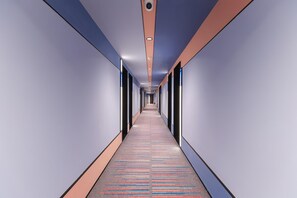 Un pasillo largo y estrecho con alfombra estampada, iluminación empotrada y una cámara de seguridad en el techo.