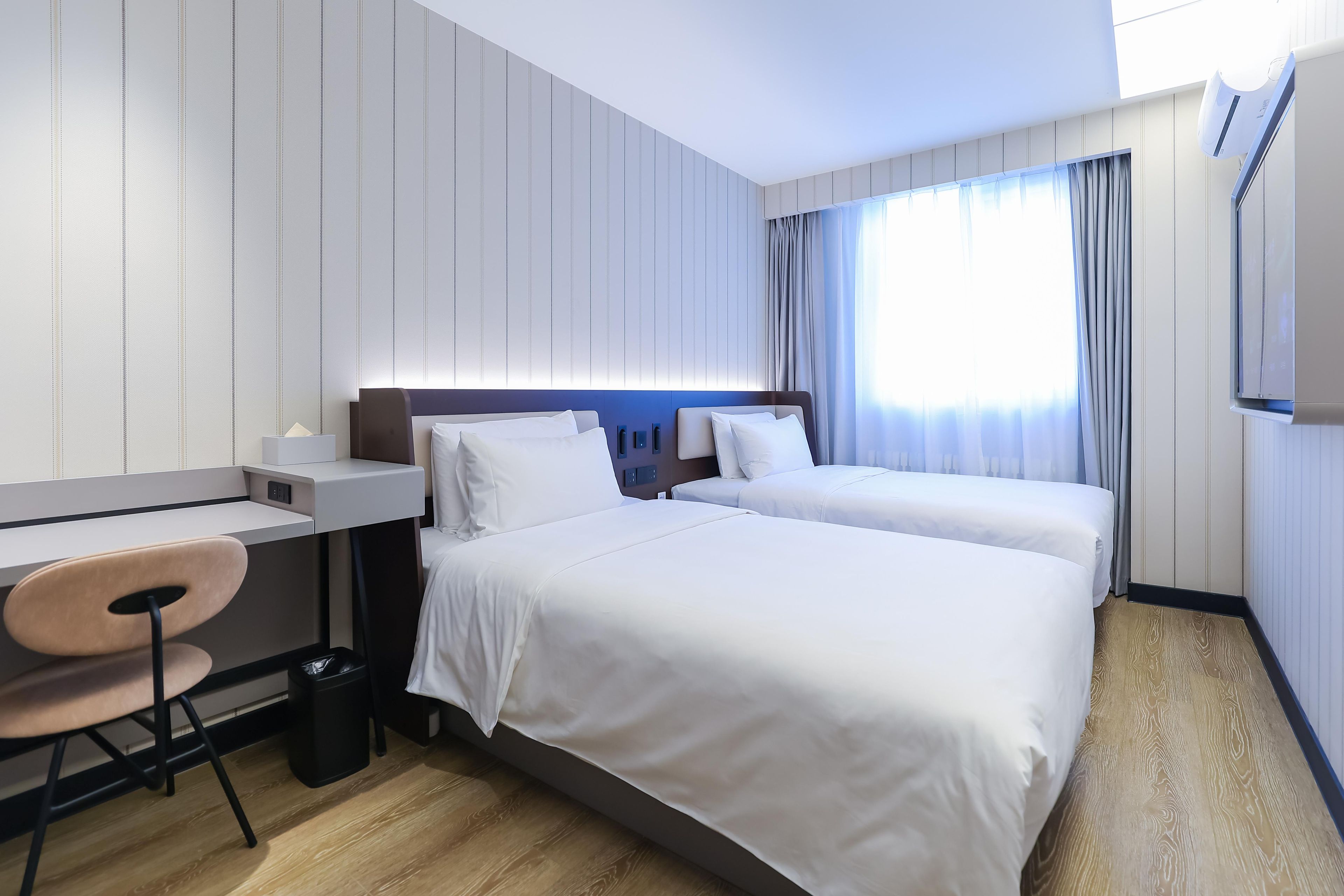 Een hotelkamer met twee bedden, een bureau, een stoel en een prullenbak.