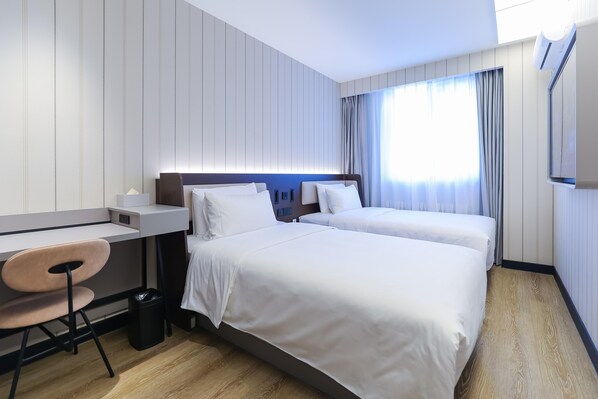 Habitación de hotel con dos camas, un escritorio, una silla y un cubo de basura.