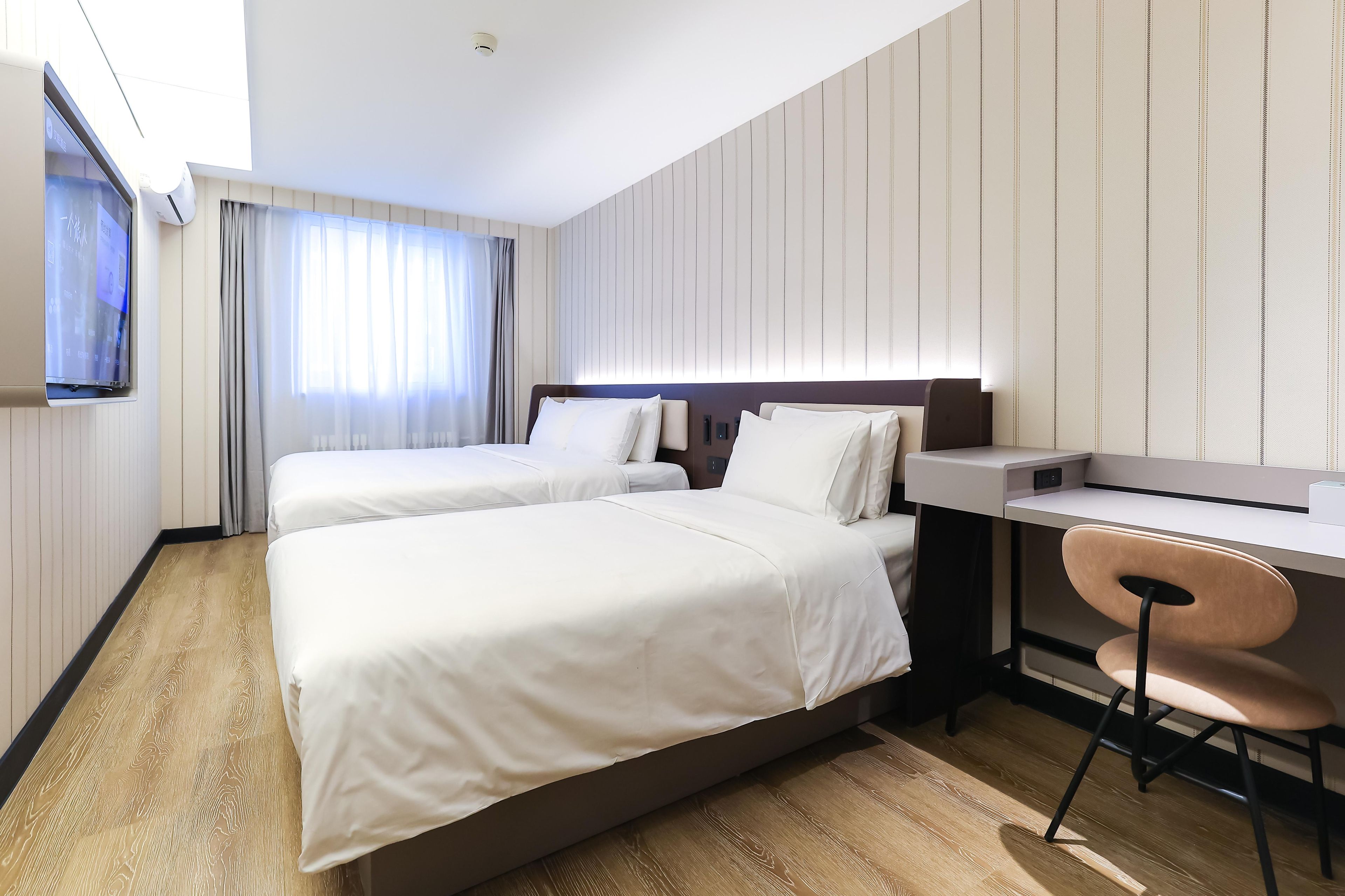 A hotel room with two beds, a desk, and a TV.