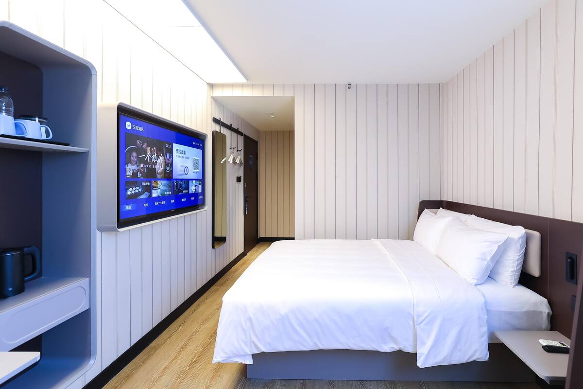 Une chambre d’hôtel moderne équipée d’un lit, d’un téléviseur fixé au mur et d’une petite table avec une télécommande.