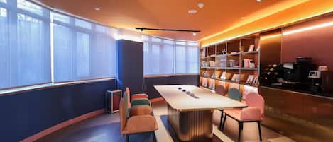 Une salle de conférence moderne équipée d’une longue table, de chaises confortables, d’une bibliothèque et d’une machine à café.