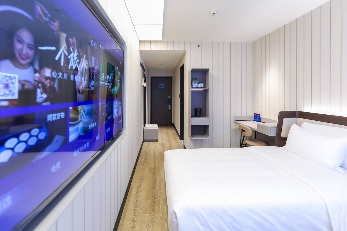 Une chambre d’hôtel équipée d’un grand écran numérique, d’un lit, d’un bureau et d’une étagère.