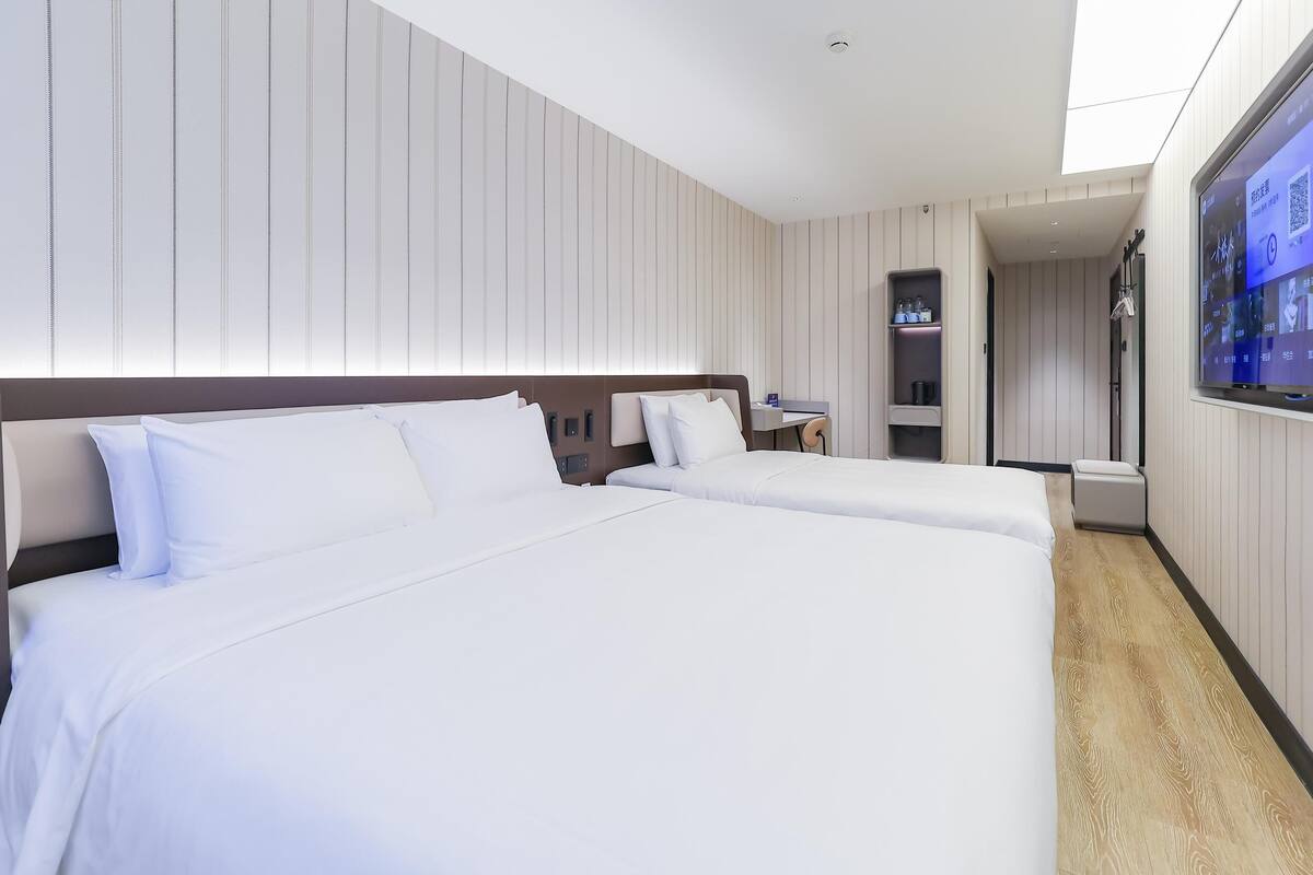 Une chambre d’hôtel avec deux lits, une télévision, une petite table et une étagère avec des articles de toilette.