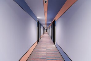 A long, narrow hallway with a patterned carpet, recessed lighting, and a security camera on the ceiling.