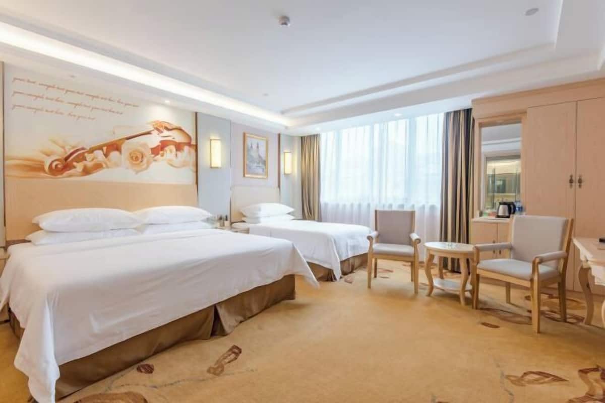 Une chambre d’hôtel avec deux lits, un bureau, une chaise et une grande fenêtre avec des rideaux.