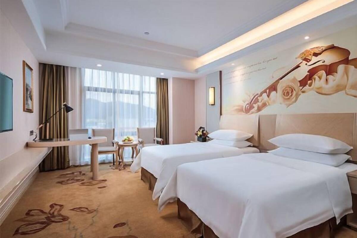 Une chambre d’hôtel avec deux lits, un bureau, une chaise, une petite table et une grande fenêtre.