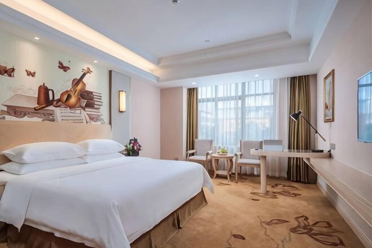 Une chambre d’hôtel avec un grand lit, un bureau, une chaise et une fenêtre avec des rideaux.