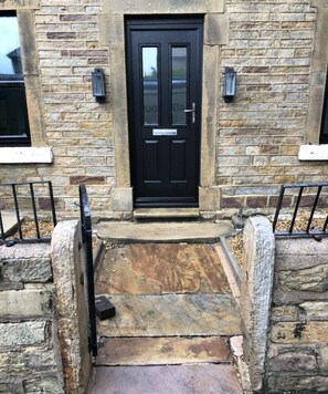 A stone building with a black door, stone steps, and metal railings.