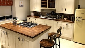 Cucina con mobili bianchi, un piano di lavoro in legno, un fornello a gas, un frigorifero e due sgabelli da bar.