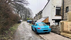 Una stretta strada sterrata, fiancheggiata da edifici residenziali e auto parcheggiate.