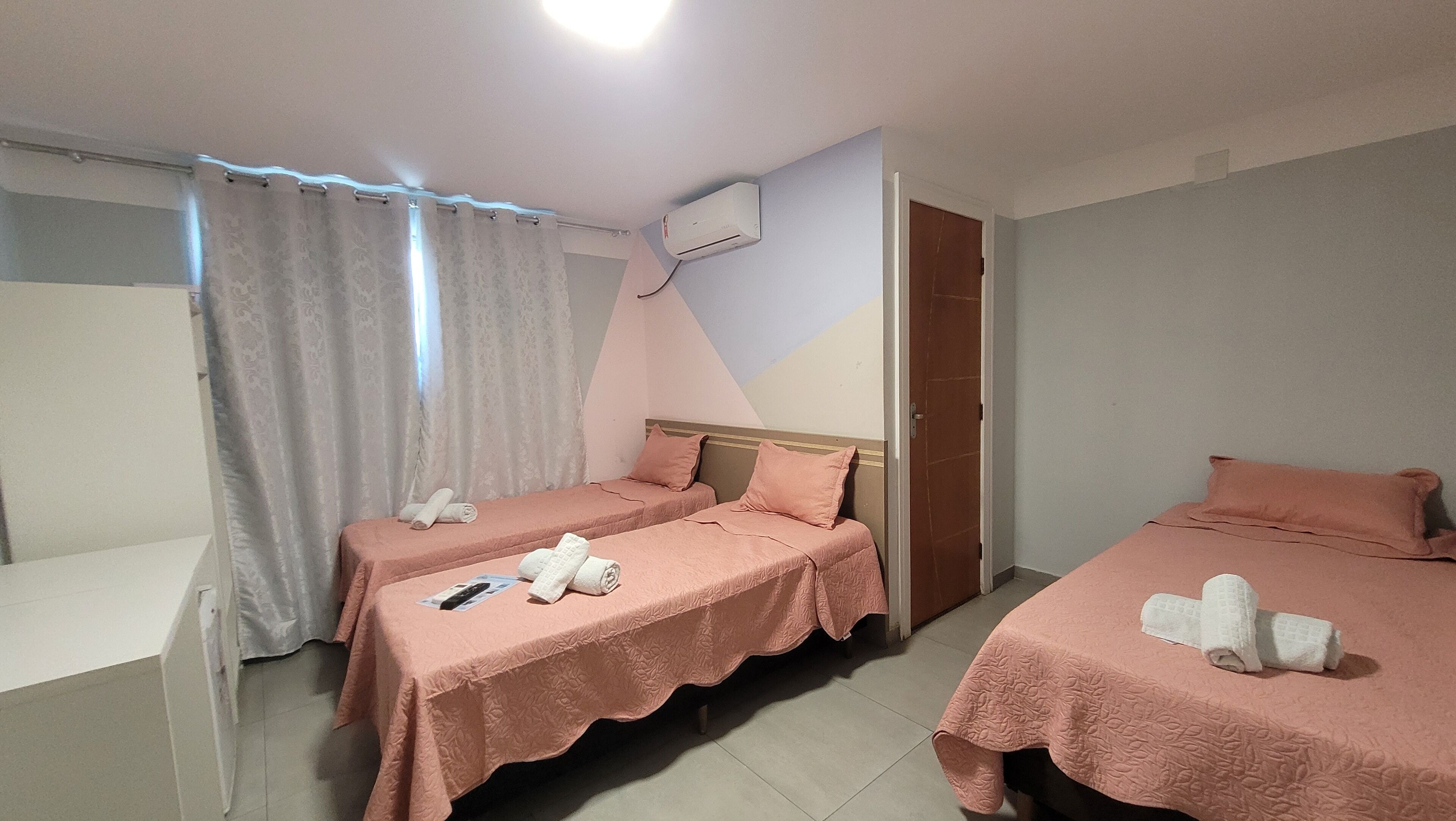 Habitación de hotel con dos camas individuales, baño con cortina de ducha y equipo de aire acondicionado en la pared.