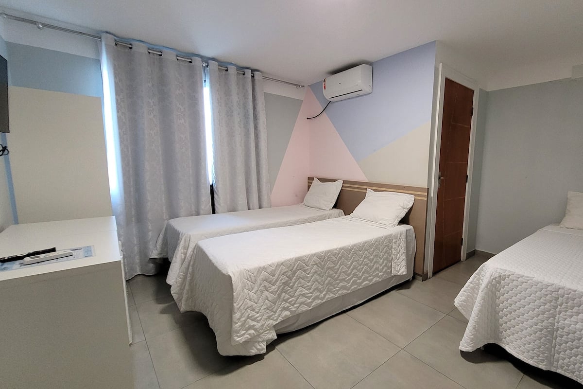 Hotellihuone, jossa on kaksi sänkyä, työpöytä ja ikkuna, jossa on verhot.