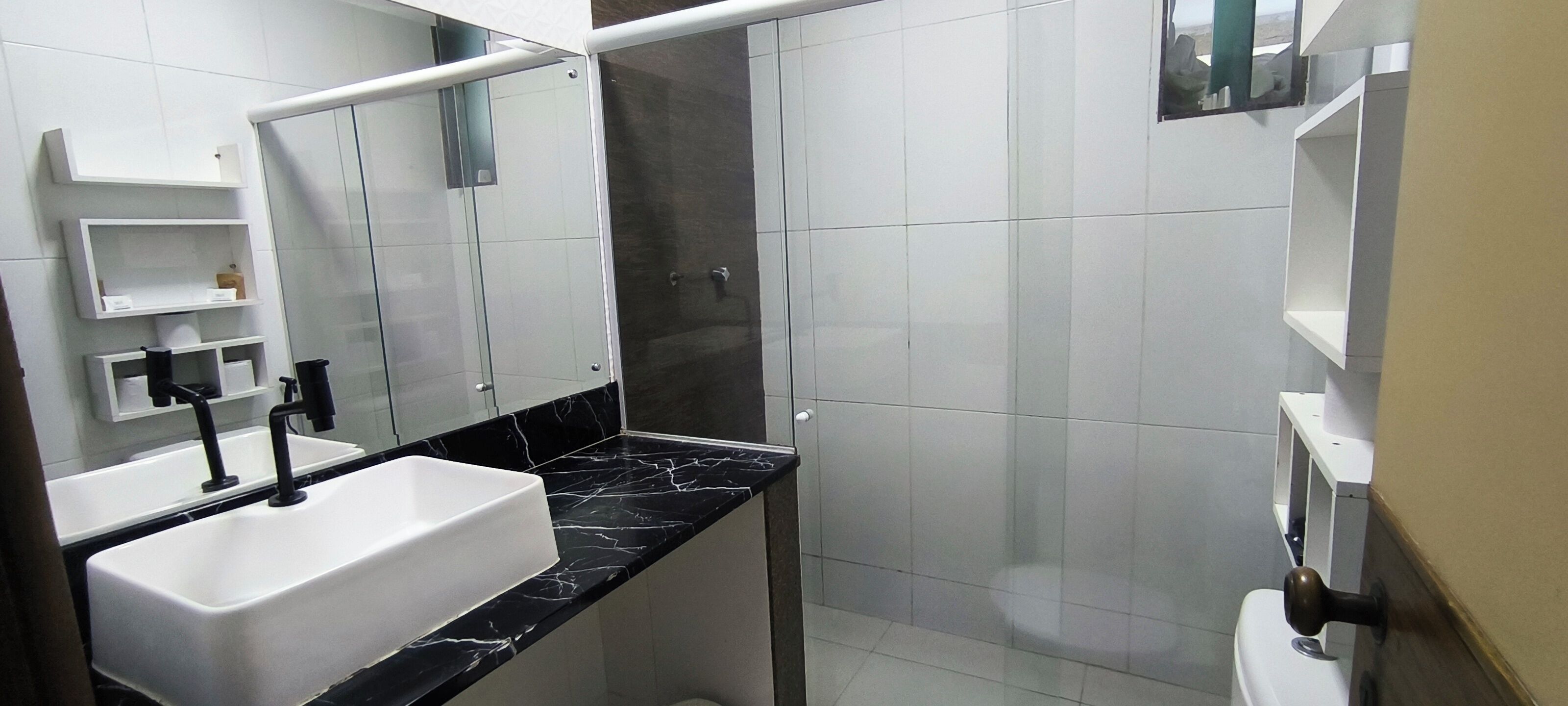 Een badkamer met een wit wastafelmeubel, een zwart aanrechtblad en een douchecabine van glas.