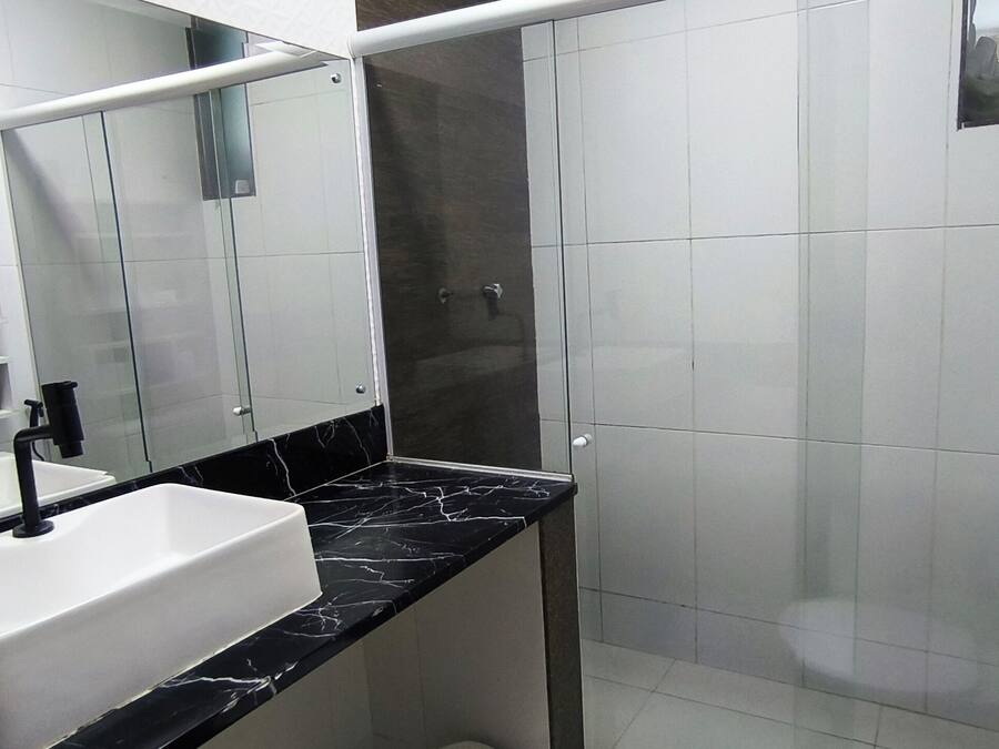 Een badkamer met een wit wastafelmeubel, een zwart aanrechtblad en een douchecabine van glas.