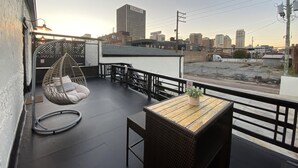 A rooftop terrace with a hanging chair, a small table with a plant, and a view of the city skyline. - Fabulous Mid-Century Loft In <3 of BHM (Birmingham)