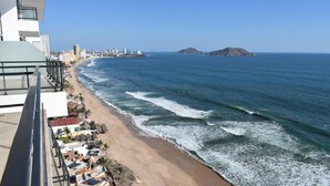 Vista costera con playa, olas del océano y un paisaje urbano al fondo.