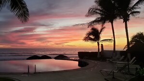 Vista al atardecer desde una zona de piscina con sillas de descanso y palmeras.