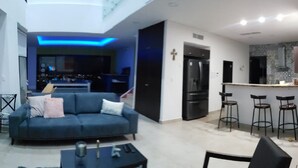 Una sala de estar moderna con un sofá azul, una mesa de centro y una zona de cocina con refrigerador y taburetes de bar.