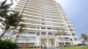 Un hotel de varios pisos con diseño moderno, que cuenta con balcones en cada planta, piscina y zonas de estar al aire libre.