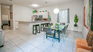 A modern kitchen with white cabinets, a dining area with a glass table and chairs, and a living room with a sofa and a plant. - Blue Ocean Vacation Rentals at Las Verandas️ ️ (South Padre Island)