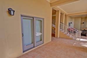 A residential building with a glass door entrance, a tiled floor, a staircase with white railings, and a small outdoor area with a red car parked nearby.
