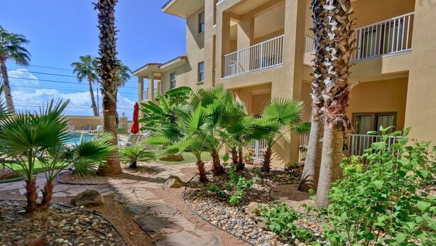 A hotel courtyard with palm trees, a pool, and a stone pathway. - Blue Ocean Vacation Rentals at Las Verandas️ ️ (South Padre Island)