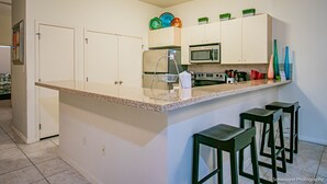 A kitchen with white cabinets, a microwave, a sink, and a bar area with stools. - Blue Ocean Vacation Rentals at Las Verandas️ ️ (South Padre Island)