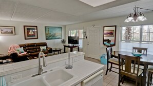 A modern kitchen with a large island, a dining area with wooden chairs, and a living room with a brown leather sofa. - Great Condo in the Middle of it ALL! (South Padre Island)