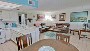 A modern living room with a dining table, sofa, and kitchen area with white cabinets and a sink. - Great Condo in the Middle of it ALL! (South Padre Island)