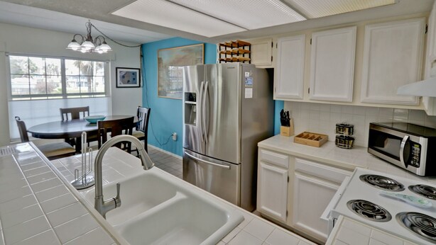 A modern kitchen with white cabinets, stainless steel appliances, and a blue accent wall. - Great Condo in the Middle of it ALL! (South Padre Island)