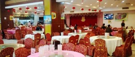 Un salón de banquetes con mesas redondas, sillas con estampado rojo y un escenario con decoraciones rojas.