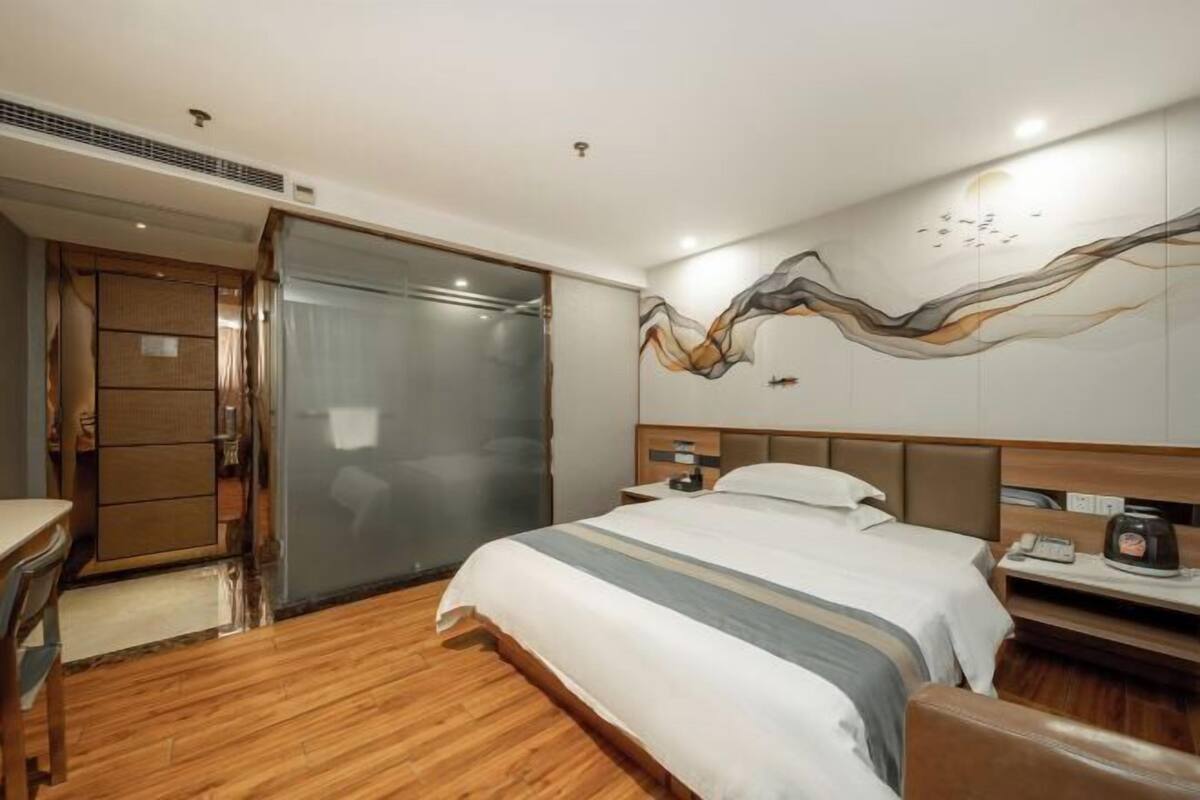 Habitación de hotel con cama, escritorio, silla, armario y zona de ducha.