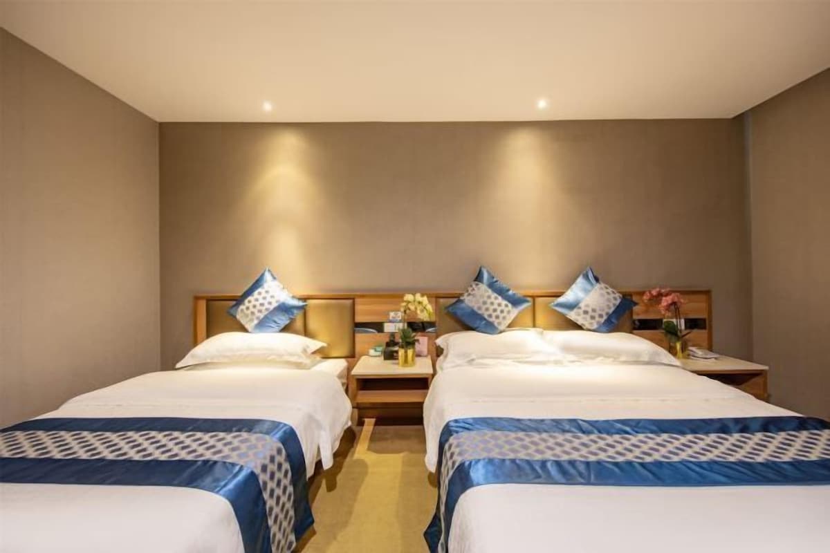 Une chambre d’hôtel avec deux lits, chacun doté d’une tête de lit, d’une table de chevet et d’une petite table sur laquelle est posé un vase de fleurs.