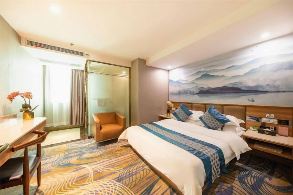 Habitación de hotel con cama, escritorio, silla, mesita de noche y un cuadro en la pared.