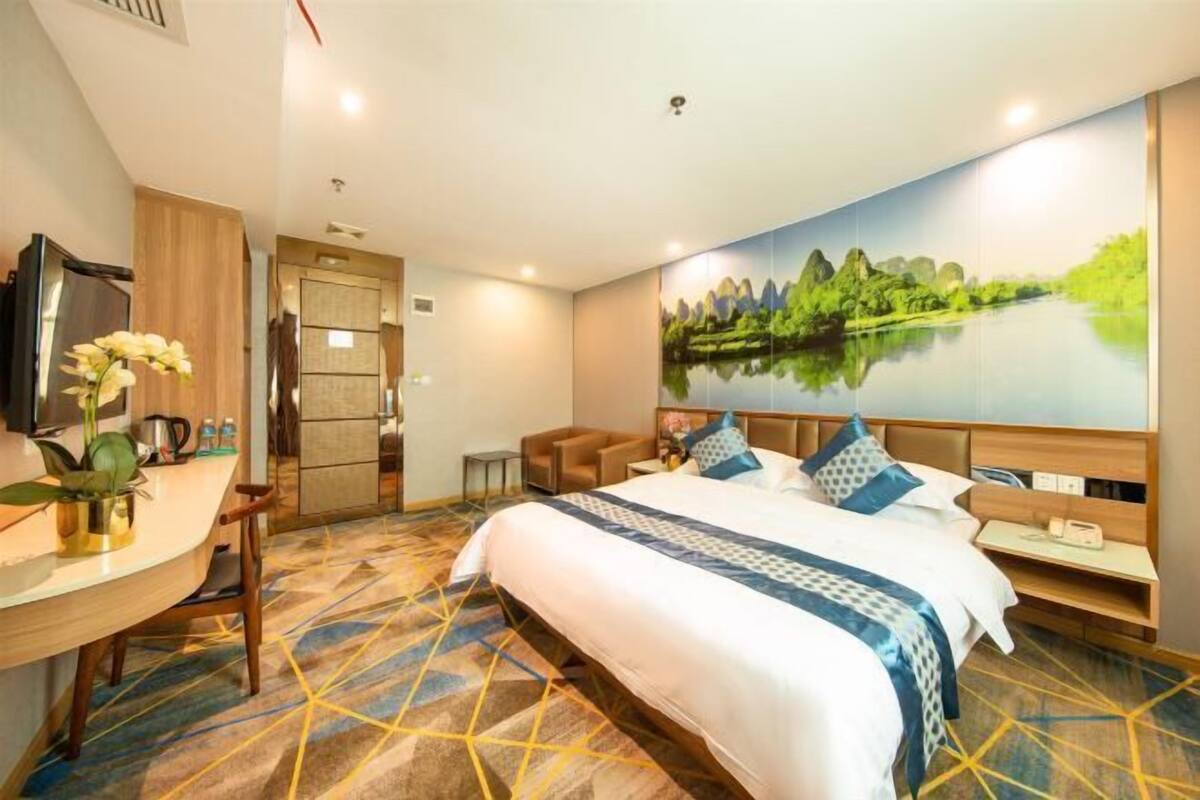 Una habitación de hotel con una cama grande, un escritorio con silla, televisión y un cuadro de un paisaje en la pared.