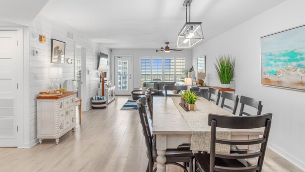 A spacious dining area with a long wooden table, black chairs, and a ceiling fan.