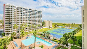 A hotel with multiple floors, a swimming pool, tennis courts, and a view of the beach.