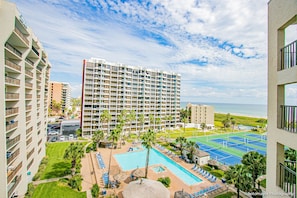 A hotel with multiple floors, a swimming pool, tennis courts, and a view of the ocean.