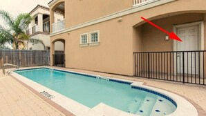 A swimming pool with a hot tub, surrounded by a beige building with balconies and a wooden fence.
