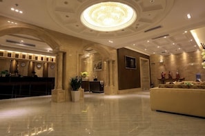 A hotel lobby with a reception desk, a large chandelier, and a reception area with a sofa. - Haihe Business Hotel (Enping)