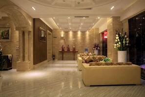 A hotel lobby with a reception desk, seating area, and a large potted plant. - Haihe Business Hotel (Enping)